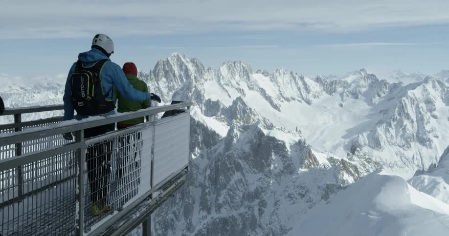 A group of people are walking to the edge of the Aiguille du Midi platform to take in a mountain view in winter