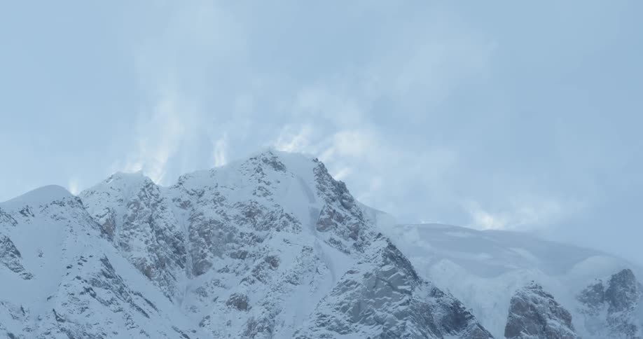 Clouds floating mostly behind some snow-covered mountains