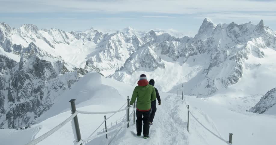 People hold onto a rope railing as they walk down a snowy ridge