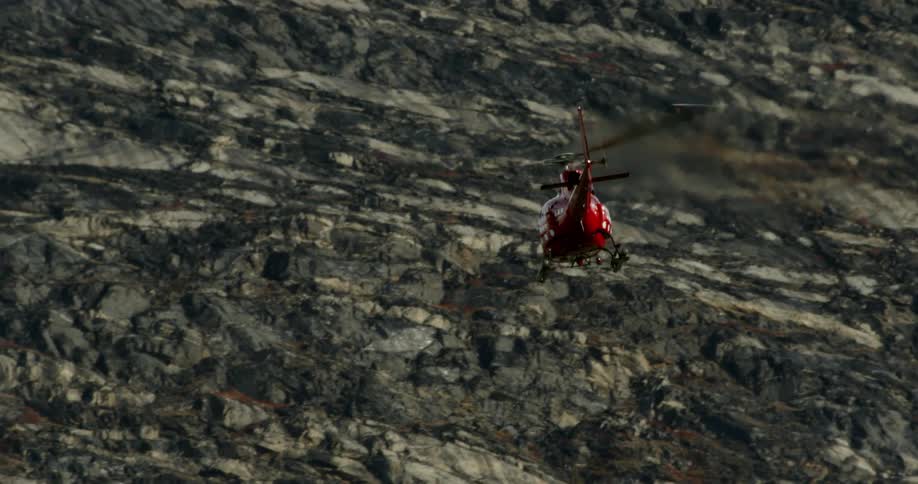 A red helicopter flies near mountains