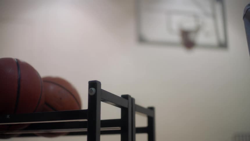 Person picks basketballs off a rack and throws them at a basketball hoop