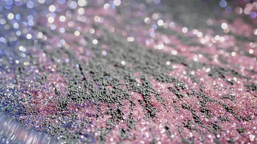 Magnetic granules and glitter are swirling and rising from a surface