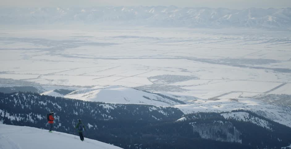 Two men stand atop a snow covered mountain