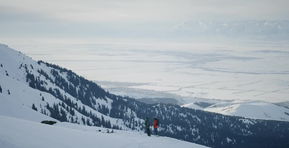Two people stand atop a snow covered mountain