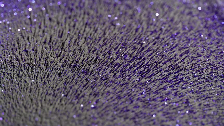 Iron filings and glitter move in a reflective liquid