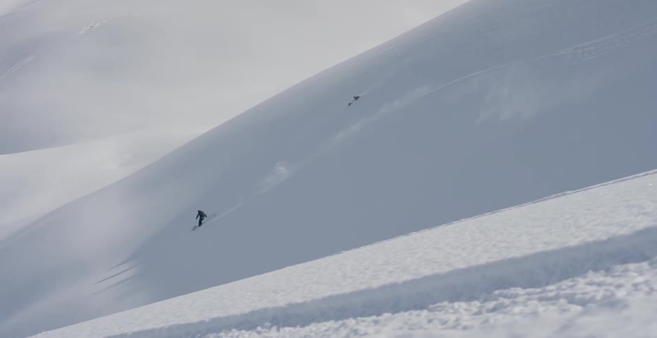 A person skis down a steep mountain slope through fresh powder