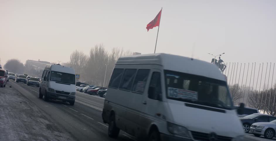 Traffic is moving on a street past a kyrgyzstan flag on a winter day