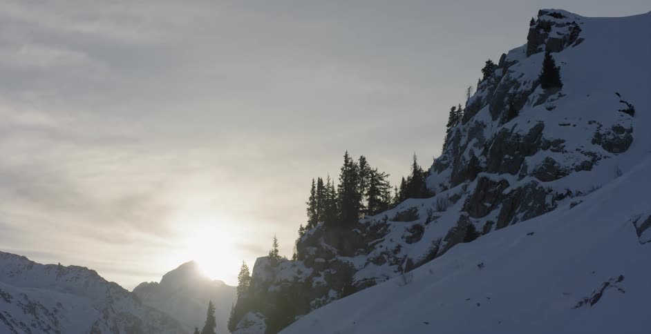 Snowy mountain and trees sit under a cloudy sky