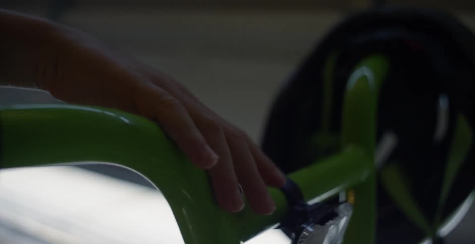 A child is running their hands over a bicycles handlebars inside a garage during the day