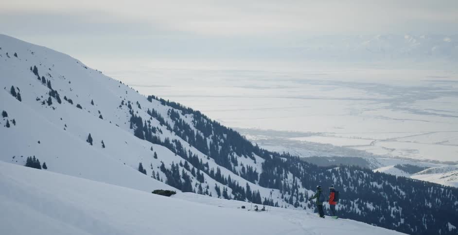 Two men stand atop a snow covered mountain