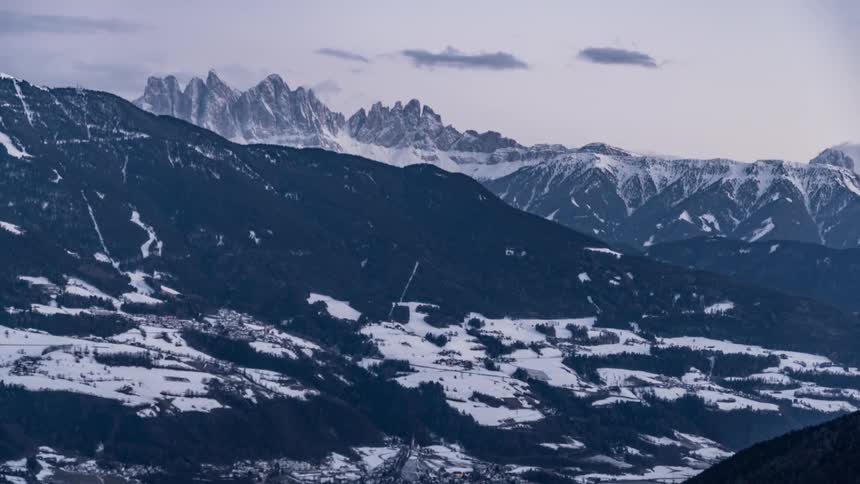 Clouds float over snowy mountains at sunrise
