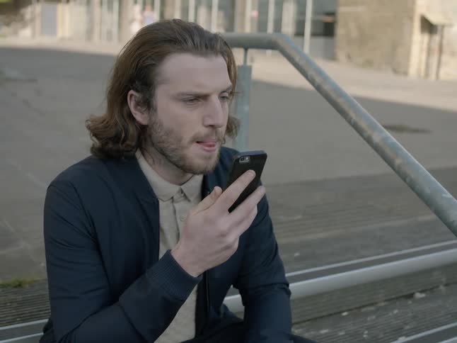 Man talks into his phone while sitting on steps outside