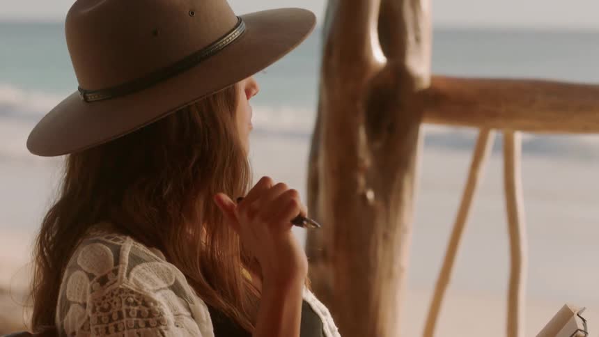 A woman sits on a beach and writes in a notebook