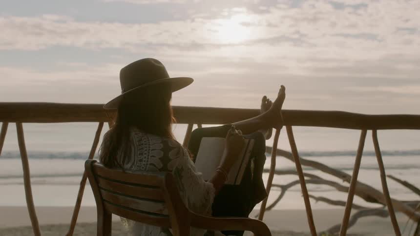 A woman sits on a deck with her feet up writing in a journal