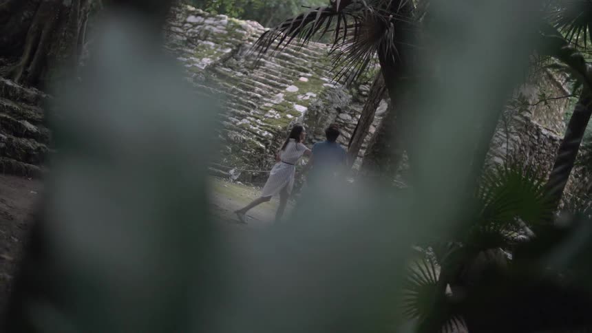 A man and woman look at ruins in a jungle