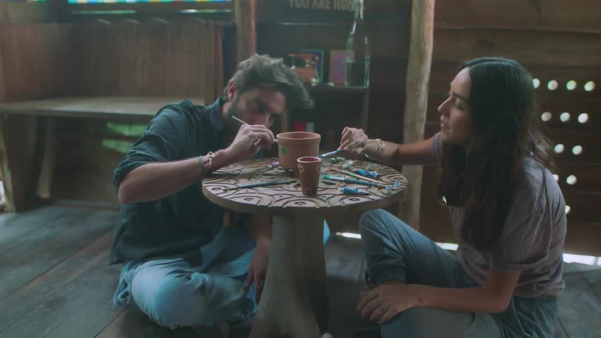 A man and woman are painting pottery together in a cottage in daylight