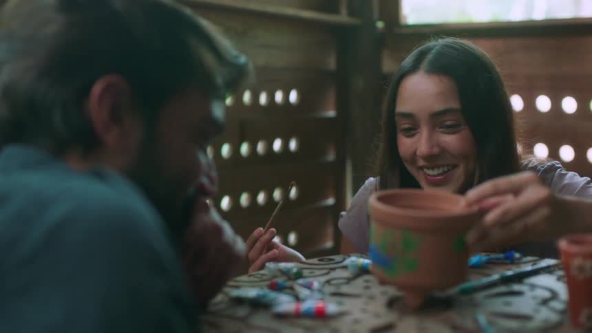 A man and woman smile while painting pottery