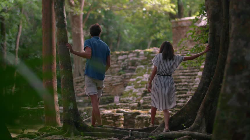 Man and woman walking past trees to a structure built in a forest