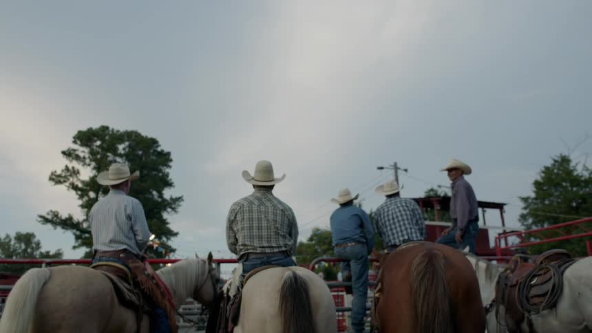 Cowboys sit on horses in a paddock