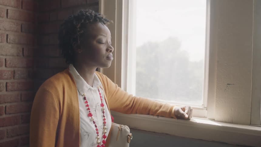 A woman is breathing deeply as she stares out a winder in a building in daylight