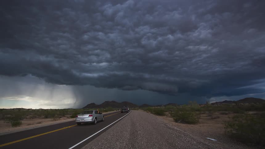 A rain storm hovers over a road running through a rural desert area