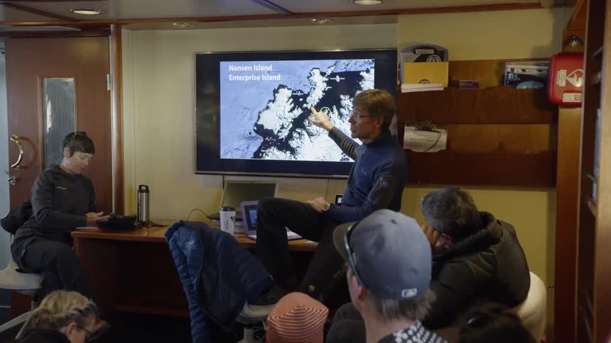 A man instructs other people using a pointer and a television screen