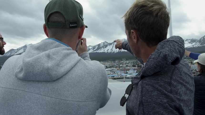 Two men pointing and looking at snowy mountains with clouds in the sky from ship