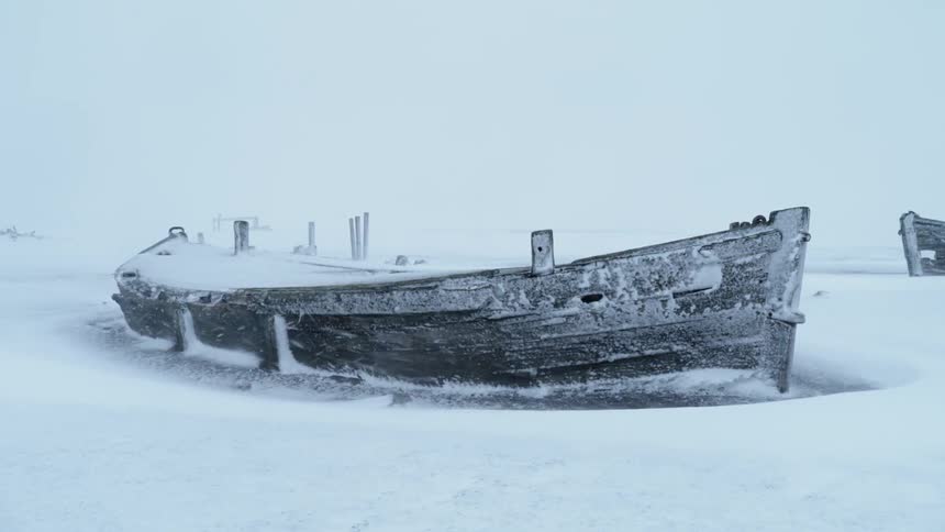 A wooden row boat is frozen to the ice sheet