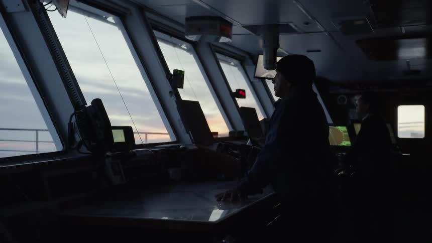 Two men look out from the captain's deck of a ship