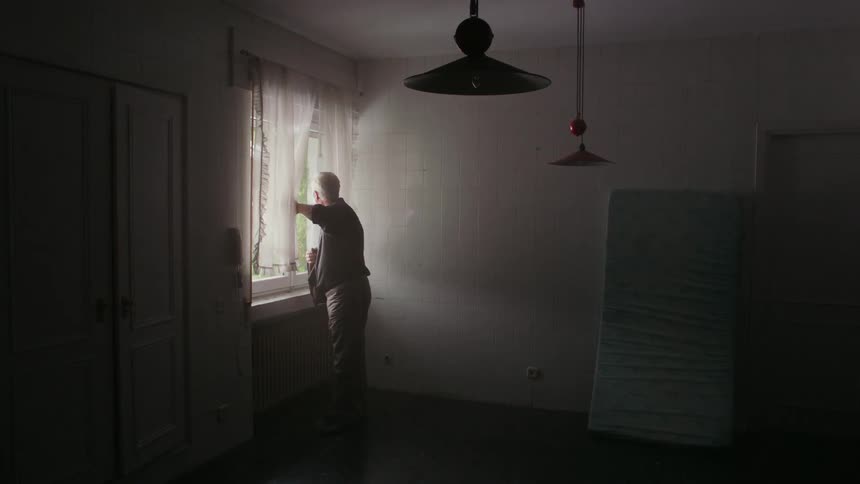 A man is opening the blinds on a window in a home in the morning