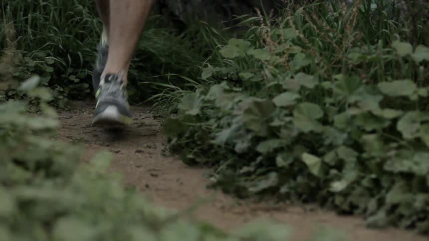 Person jogs down a small dirt path surrounded by grass and bushes