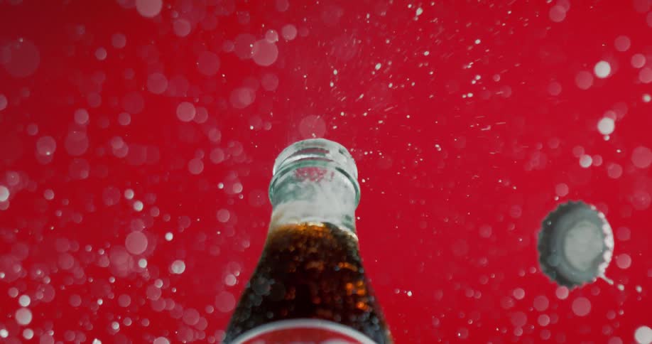 A bottle cap explodes off of a cola bottle
