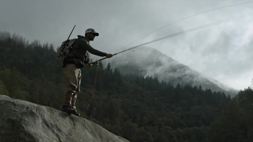 A man fishes from a boulder in the mountains