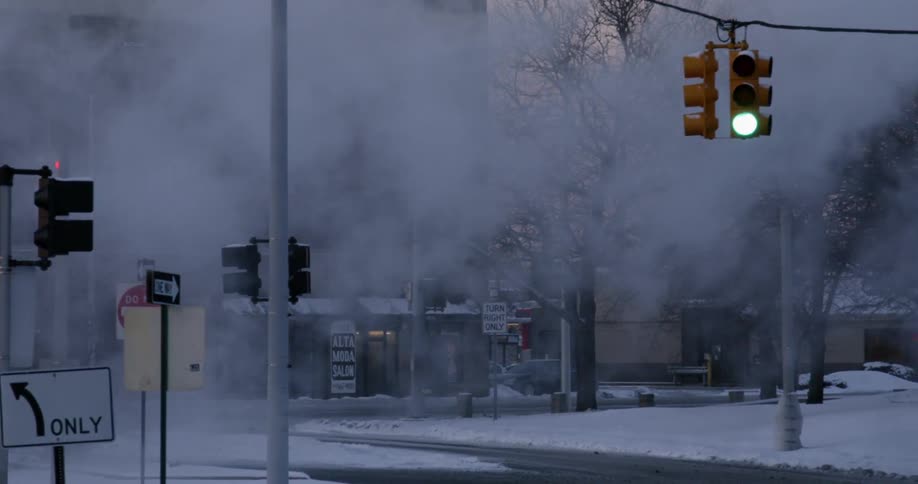 Steam is drifting across an urban intersection in winter at dusk