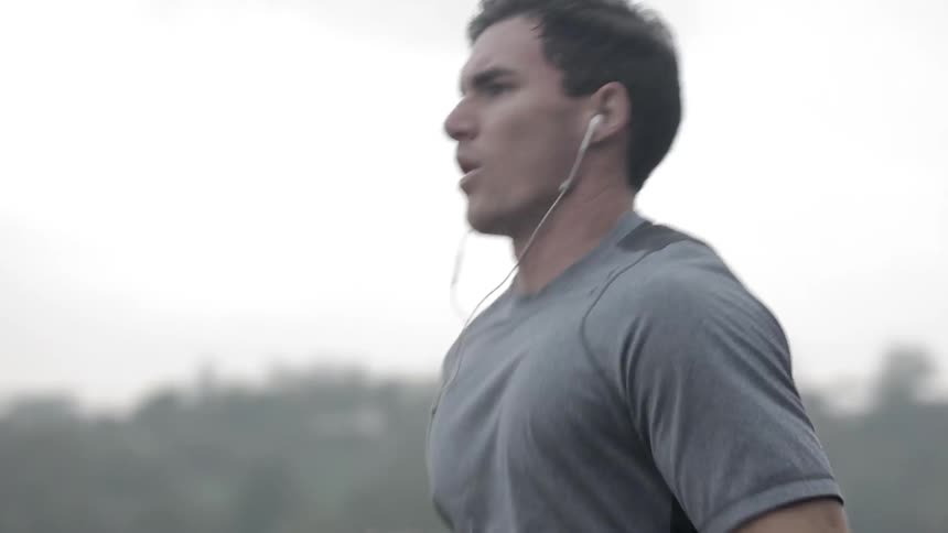 Man wears earbuds as he jogs near the trees
