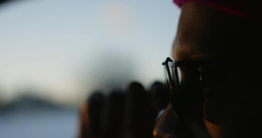 A man lowers the shades on his glasses while standing outside at dusk