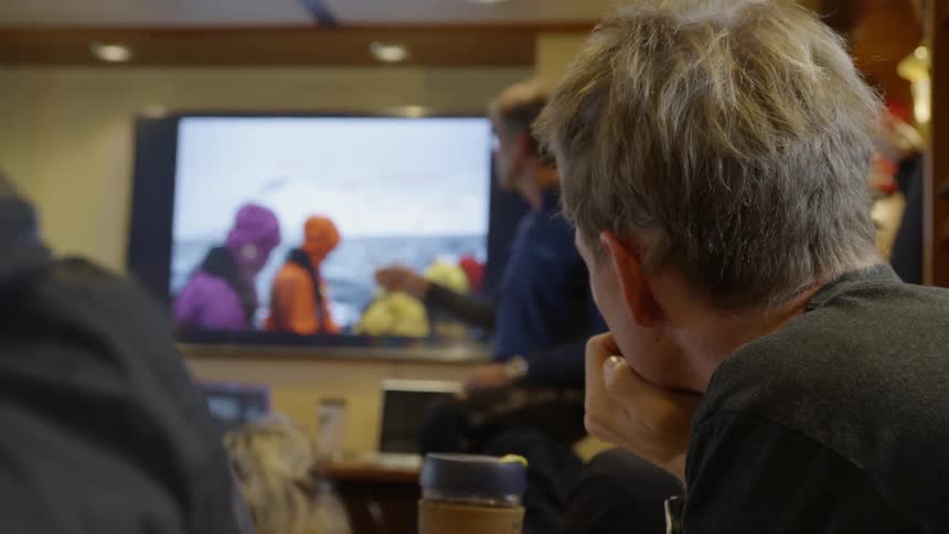 A man instructs other people using a pointer and a television screen