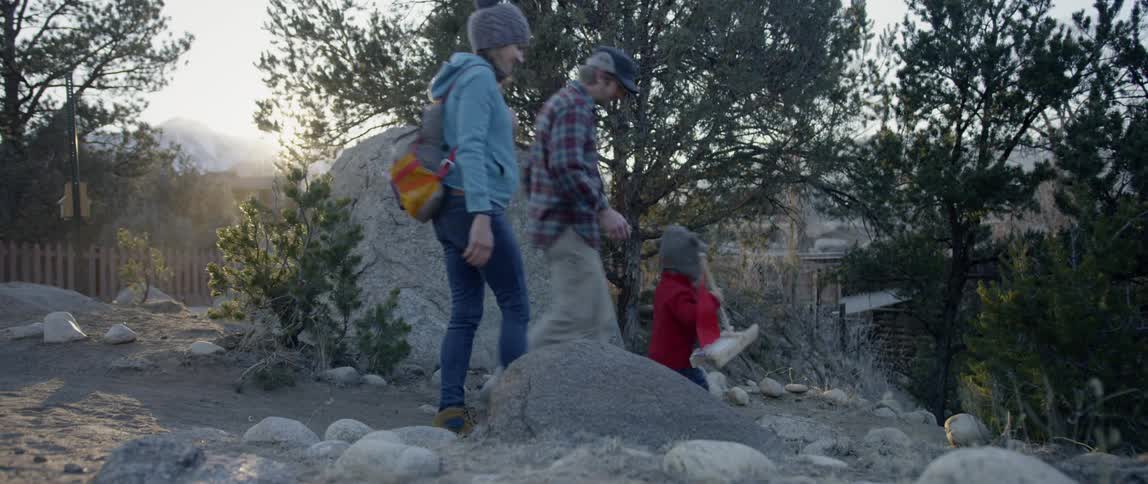 Man woman and small child walk by a large rock