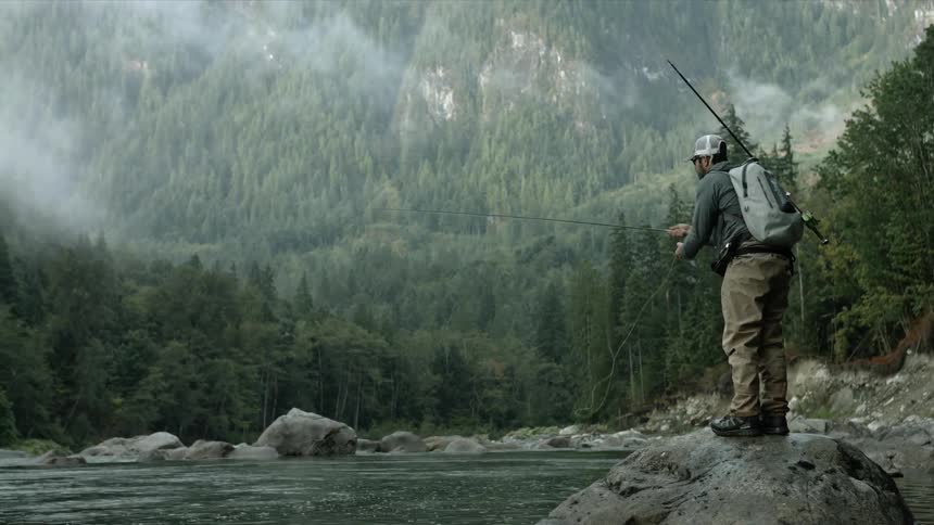 A man is standing on a boulder fishing in a river in daylight