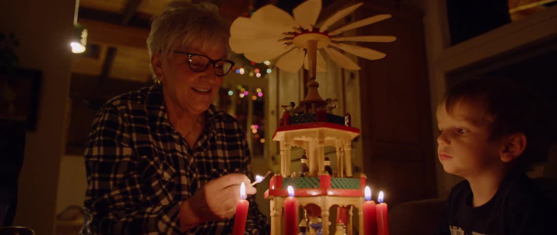A woman is lighting the candles on a christmas decoration as a boy watches