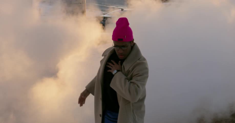 A man dances in front of steam in a city