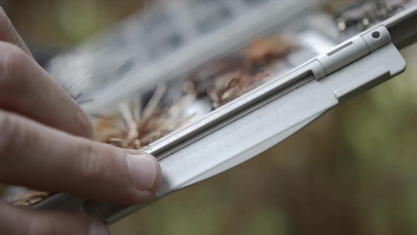 A fisherman selects a hook from a case