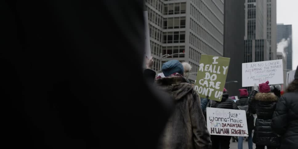 Protesters holding signs are marching down a city street in winter