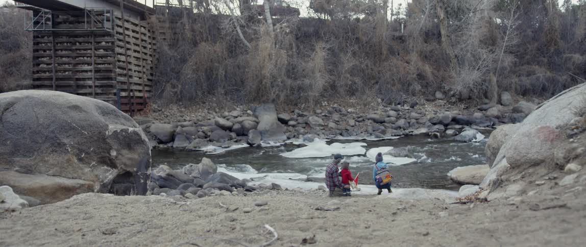 A family crouches next to an icy river