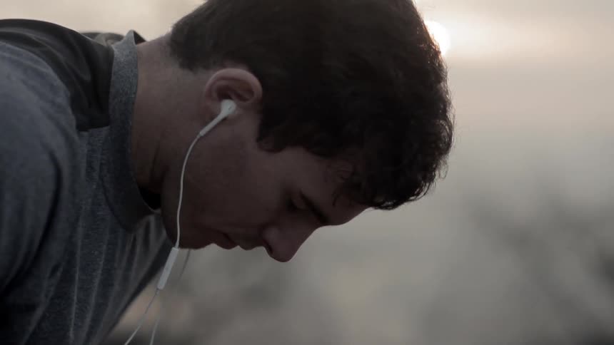 A man wears headphones while taking a break from running outside