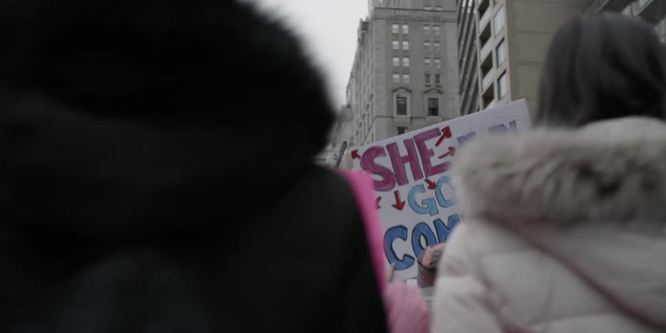 Large group of people walk through a city carrying signs and protesting