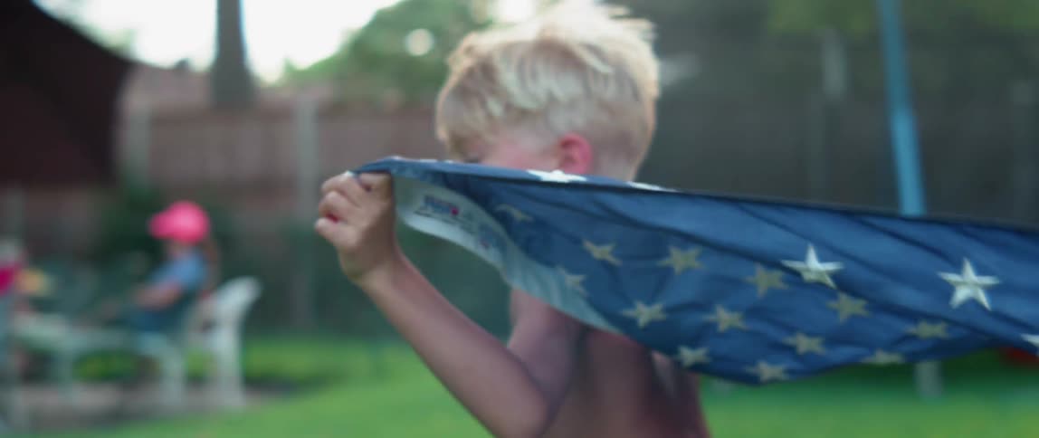 A young boy is running with an american flag in his backyard at dusk