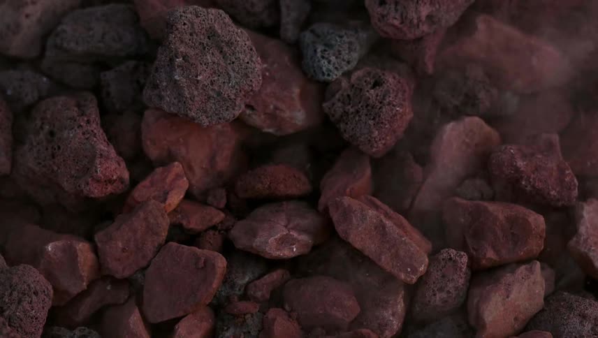 Rocks are tumbling into a pile as smoke blows across them in daylight