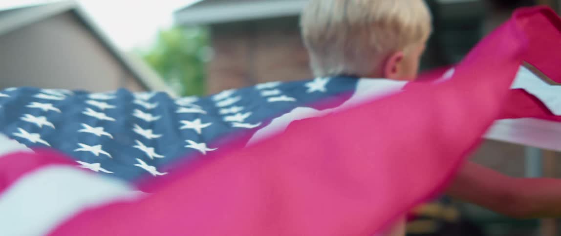 A young boy runs outside while holding an american flag