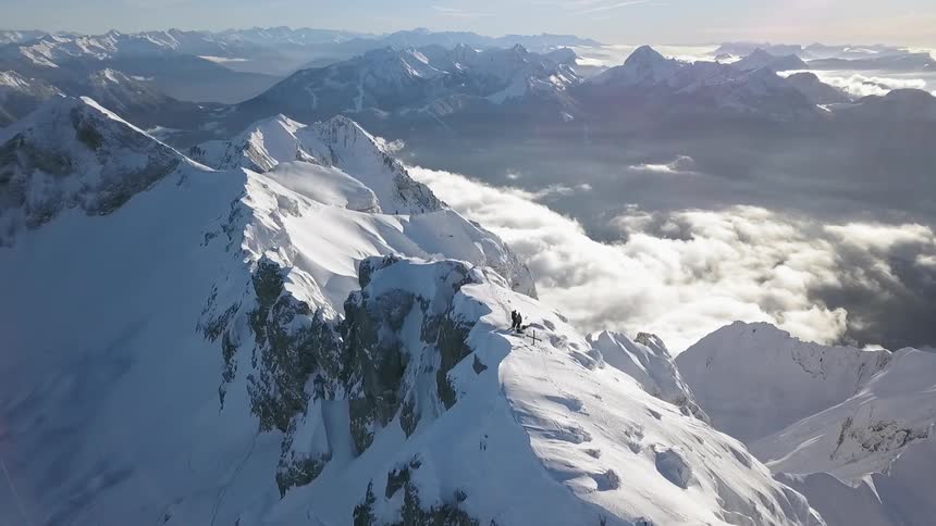 People are standing atop a mountain ridge in a snow-covered mountain range in daylight